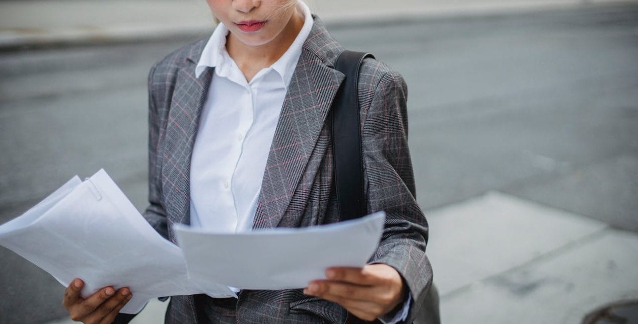 Focused businesswoman in a suit reviews important papers outdoors.