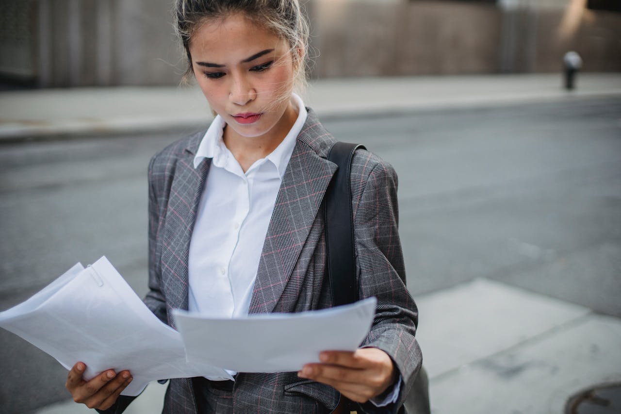 Focused businesswoman in a suit reviews important papers outdoors.
